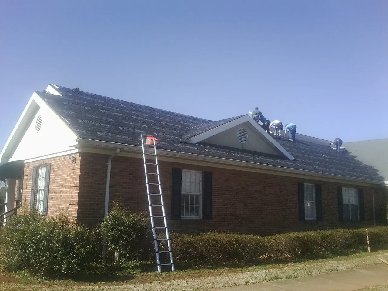 Crew tearing shingles off a brick ranch roof with a ladder set — Metal Roof Repair work by our crew in Clearwater
