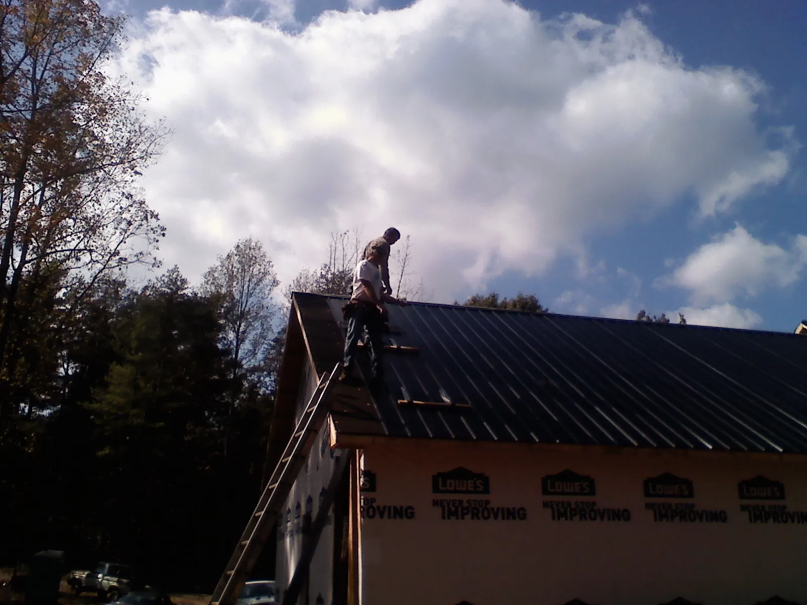 Roofer fastening dark metal panels high against a cloudy sky, from a Roof Inspection job in Clearwater